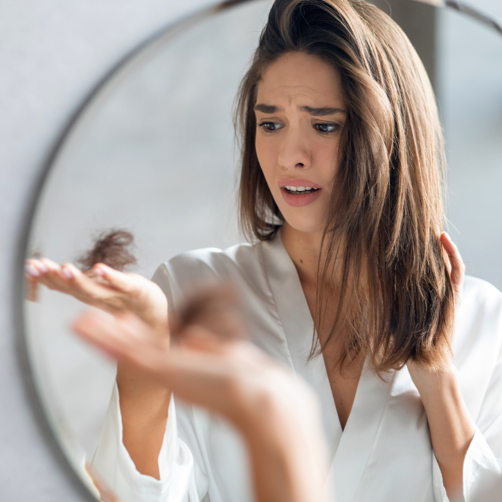 Female looking at her hair loss in her hand, looking horrified.